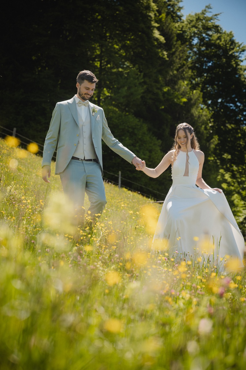 Brautpaar geht Hand in Hand durch eine sonnige Blumenwiese im Pinzgau